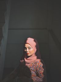 Portrait of woman wearing hijab standing against wall