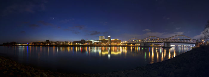 Illuminated city by river against sky at night