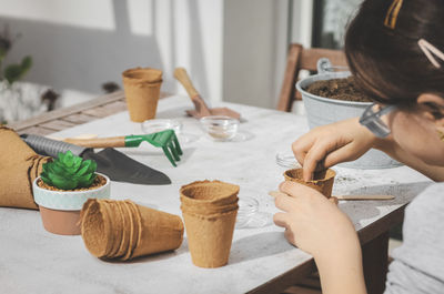 Caucasian girl planting seeds in a cardboard cup pushing her finger.