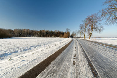 Road on snow covered landscape against clear sky