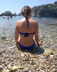 Rear view of woman in bikini sitting on beach