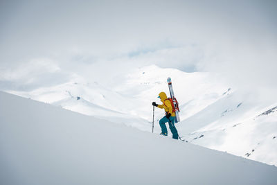 A person walks up a mountain ridge with skis on her back