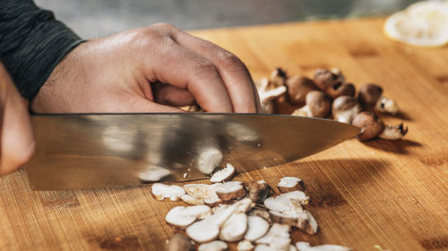 Chef cutting shiitake mushrooms with knife on a wooden cutting board
