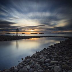 Ghost standing on shore against cloudy sky during sunset