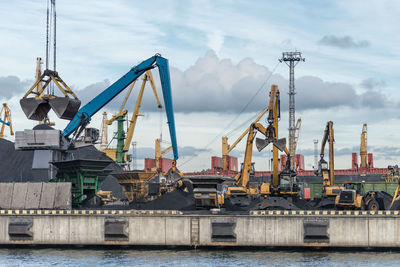 Cranes at harbor against sky