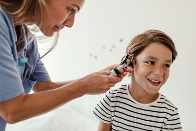 Doctor examining boy's ear with otoscope in medical examination room