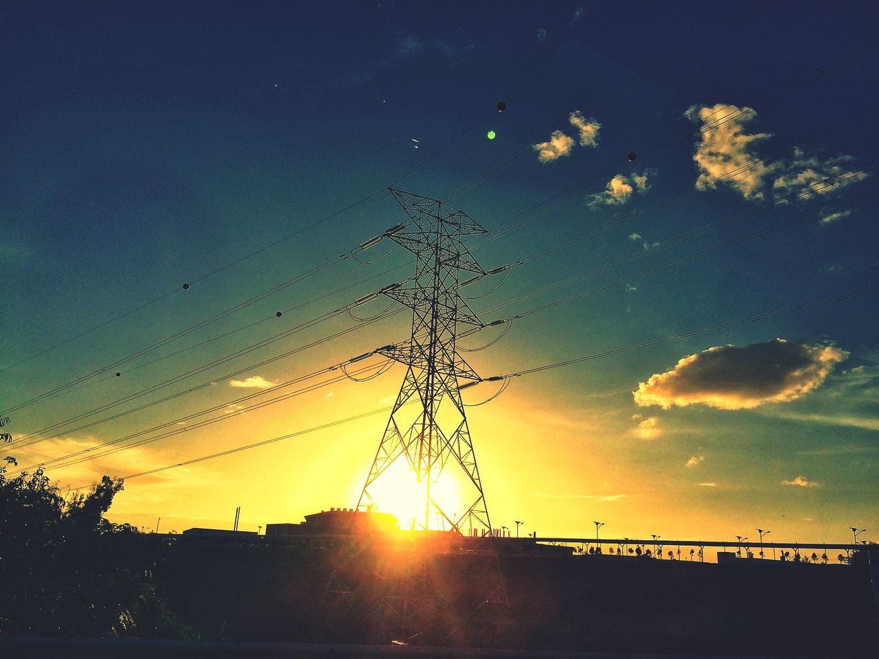 sunset, silhouette, sun, sky, orange color, power line, low angle view, beauty in nature, electricity pylon, built structure, sunlight, scenics, nature, cloud - sky, connection, architecture, tranquility, electricity, building exterior, outdoors