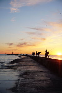 Silhouette people on beach against sky during sunset