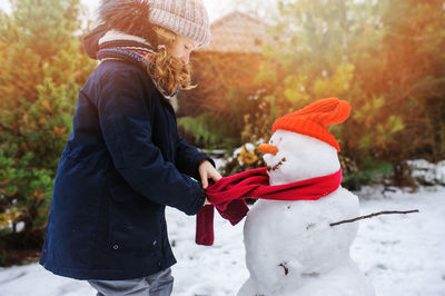 Side view of girl making snowman during winter