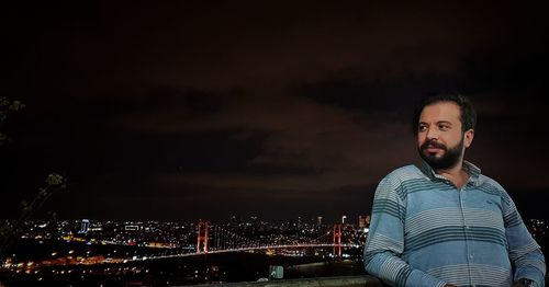 Smiling bearded man standing against illuminated cityscape at night