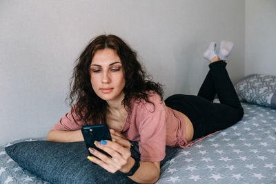 Young woman using mobile phone while sitting on bed at home