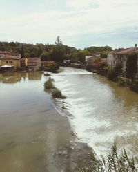 Buildings by river against sky in city