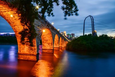 Illuminated bridge over river at dusk