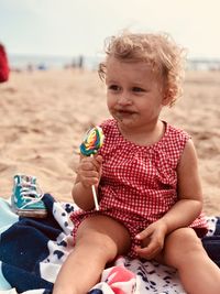 Cute girl eating lollipop while sitting at beach