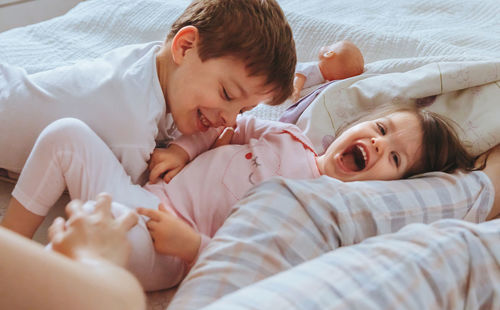Cheerful mother playing with son and daughter while lying on bed at home