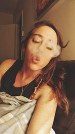 Close-up of young woman exhaling smoke on bed