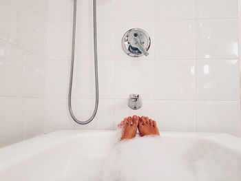 Low section of woman bathing in bathtub against wall