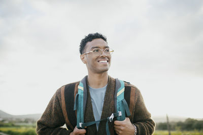 Smiling young man with backpack hiking under sky