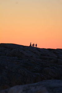 People on rocks against clear sky during sunset