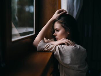 Side view of woman looking through window