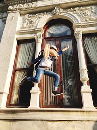 Low angle view of woman with legs apart jumping against building