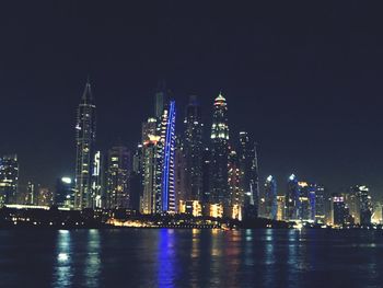 Illuminated buildings by river against sky at night