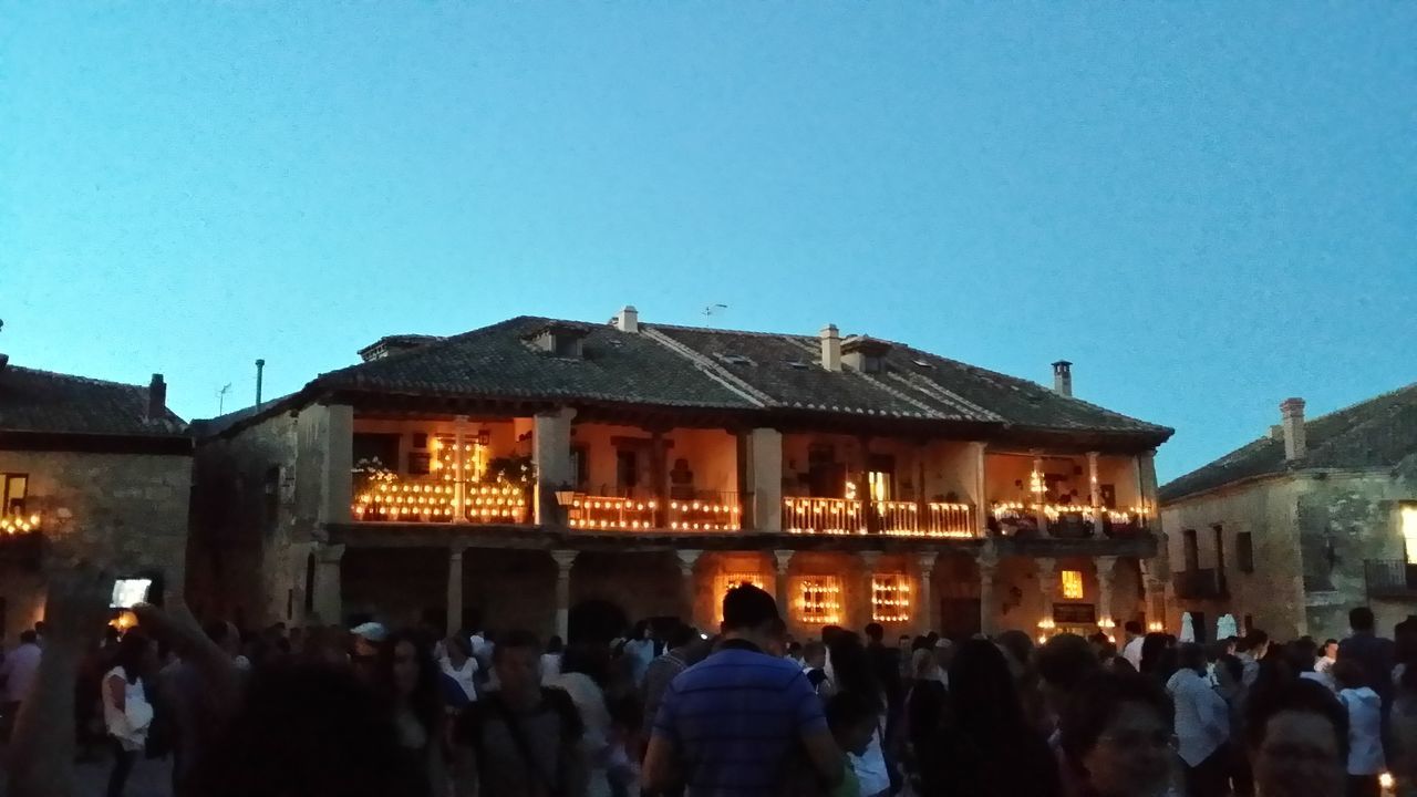 architecture, built structure, building exterior, large group of people, clear sky, illuminated, men, copy space, lifestyles, person, blue, night, city, leisure activity, dusk, city life, sky, crowd, outdoors