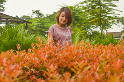 Smiling young woman standing against plants