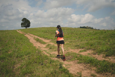 Rear view of woman walking on field against sky