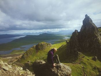 Man sitting on rock against sky