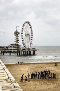 People at amusement park by sea against sky