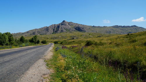 Road leading towards mountains against blue sky