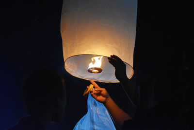 Friends igniting paper lantern at night