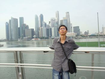 Portrait of smiling young woman standing on railing against cityscape