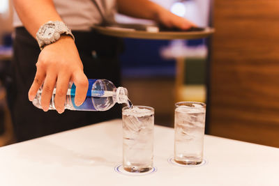 Waiter hand pouring water from bottel into a glass in restaurant.