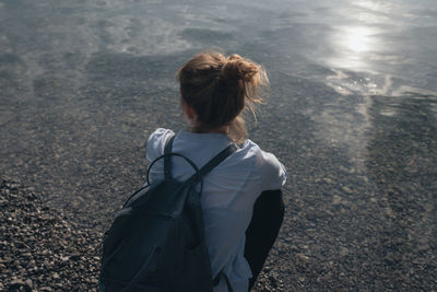 Rear view of woman with backpack crouching on shore at beach during sunny day