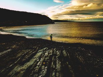 Person standing on sea shore against sky during sunset