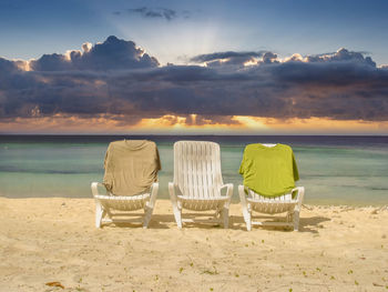 Chairs on beach against sky during sunset