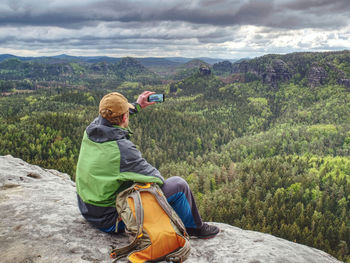 Man tourist in nature. spring free day in rocky mountains. hiker with sporty backpack stand on rock