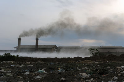 Smoke emitting from factory against sky