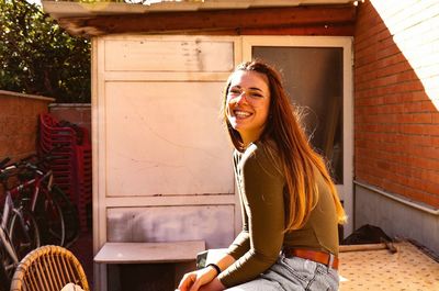 Portrait of woman wearing sunglasses while sitting by house in yard