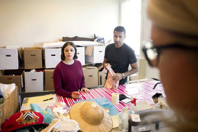 Volunteers looking at objects while standing against stack of boxes