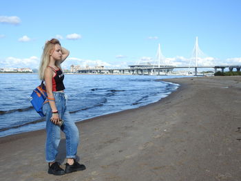 Young woman standing on bridge over sea against sky