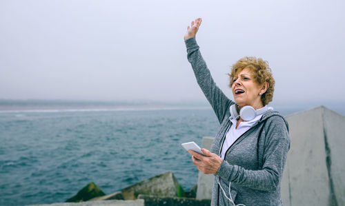 Woman using mobile phone while gesturing at beach against sky