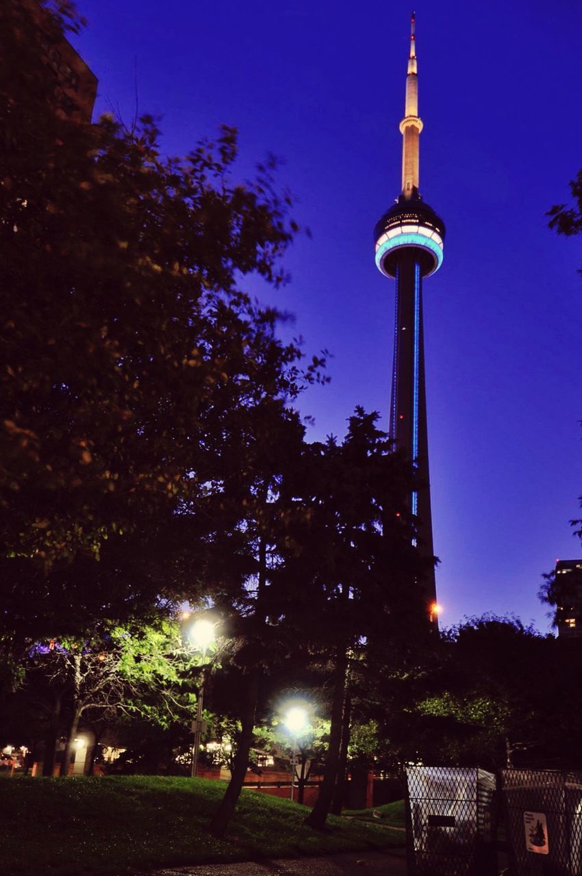 LOW ANGLE VIEW OF ILLUMINATED TOWER AMIDST BUILDINGS AGAINST SKY