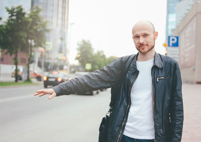 Portrait of young man hailing taxi while standing on road