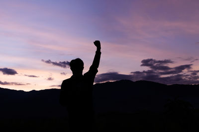 Silhouette man standing on rock against sky during sunset