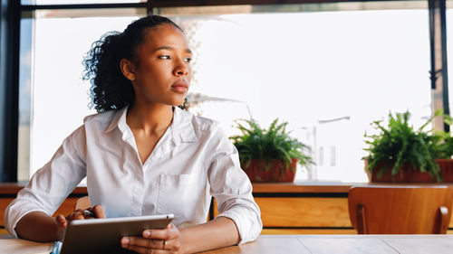 Young woman looking away while sitting on laptop