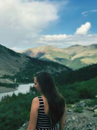 Rear view of young woman standing on mountain against cloudy sky