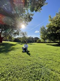 Man sitting on field against sky on sunny day